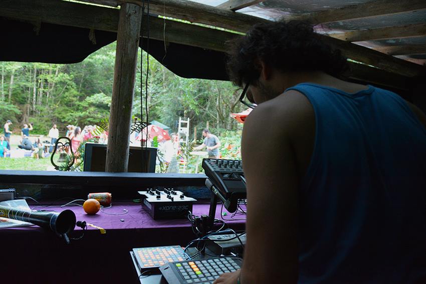 Person in a dj booth looks down at gear while people set up decor outside